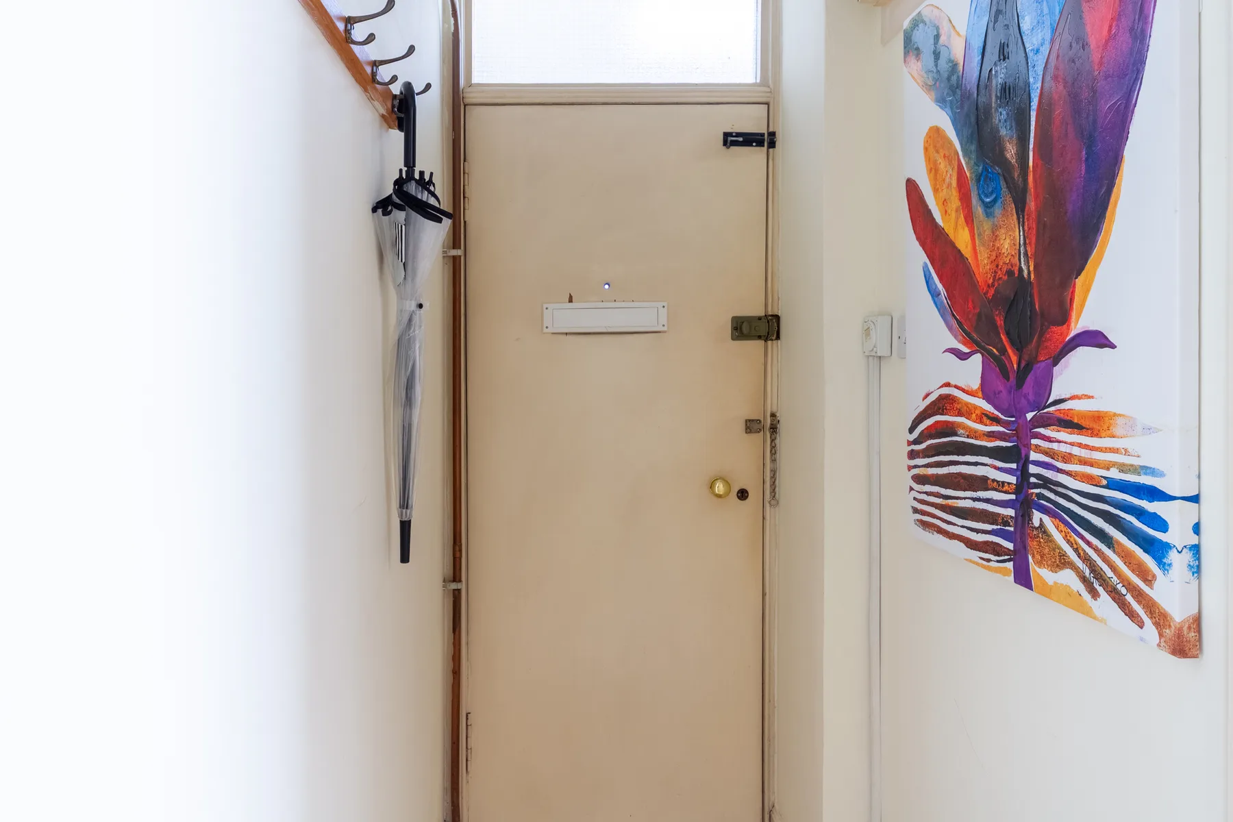 An entryway with a beige door and colorful wall art.