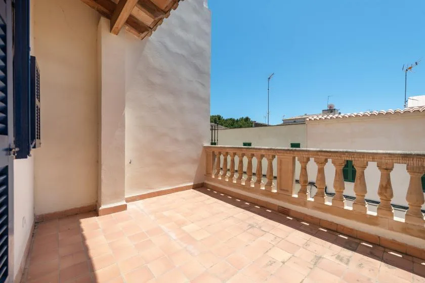 A sunlit terrace with tiled flooring and a balustrade overlooking nearby rooftops.