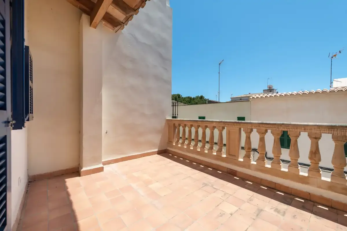 A sunny terrace with tiled flooring and a balustrade overlooks nearby rooftops.
