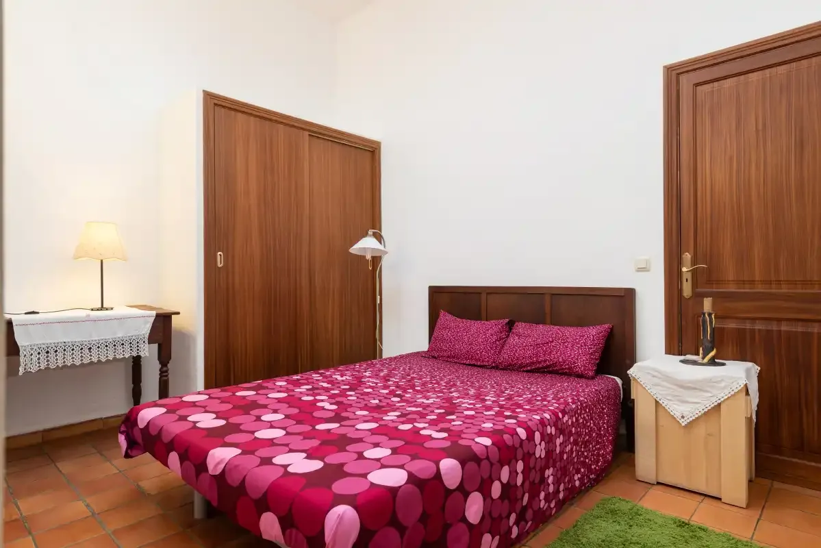 A bedroom with a bed covered in a pink patterned bedspread.