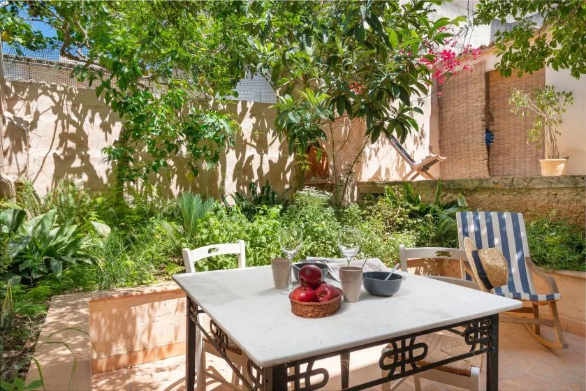 Un patio ajardinado con una mesa entre plantas frondosas y árboles.