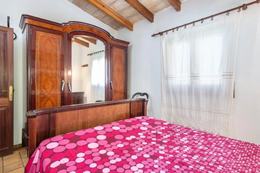 A bedroom with a bed covered in a bright pink patterned bedspread.