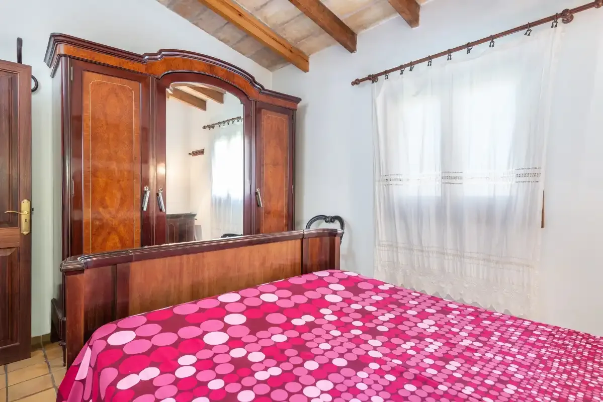A bedroom with a wooden wardrobe and a bed covered in a pink patterned bedspread.