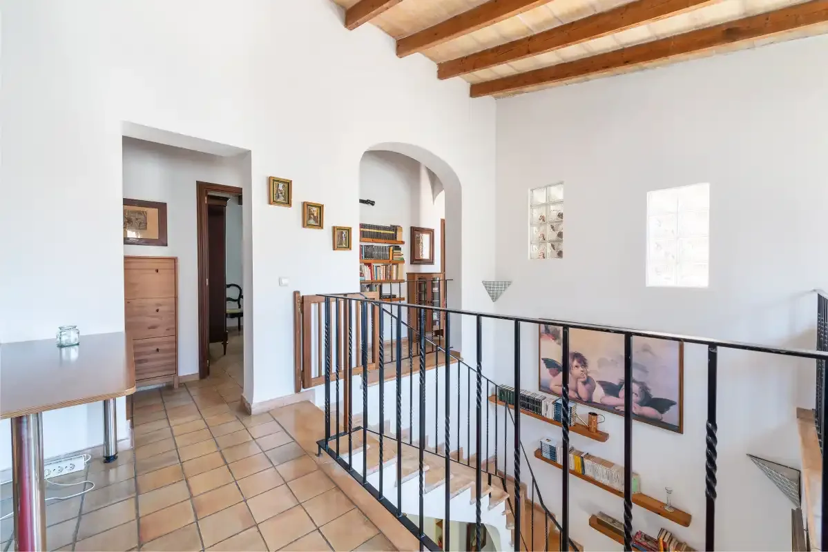 A bright interior hallway overlooks a stairwell with a black metal railing.