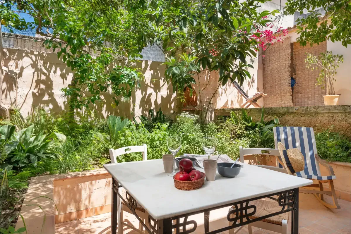 A shaded garden patio with a dining table and striped outdoor seating.