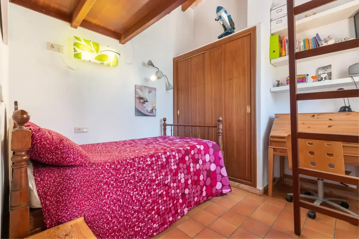 A bedroom with a single bed, wooden door, and desk.