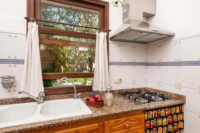 A tiled kitchen with a sink, countertop, and gas cooktop beneath a window.