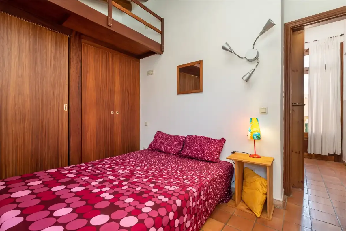 A bedroom with a patterned bed, wooden wardrobes, and a small bedside table.