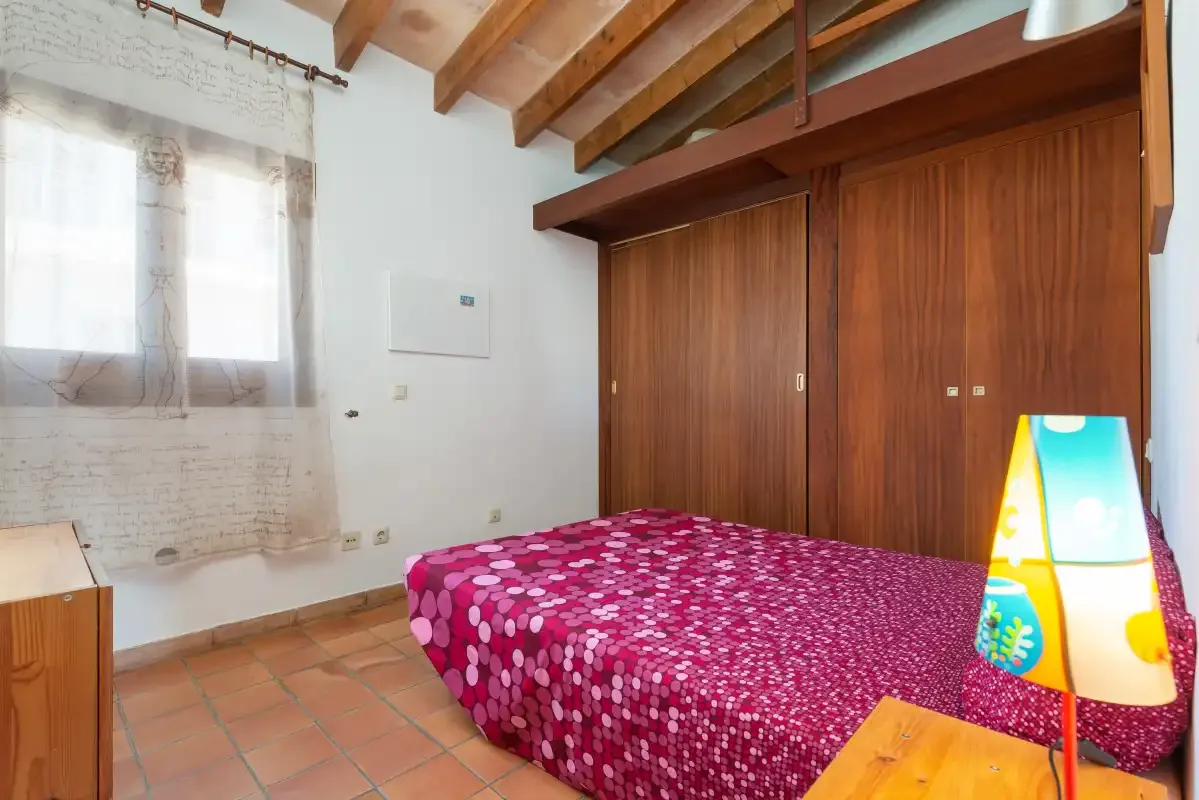 A bedroom with a bed, wooden wardrobes, and a window.