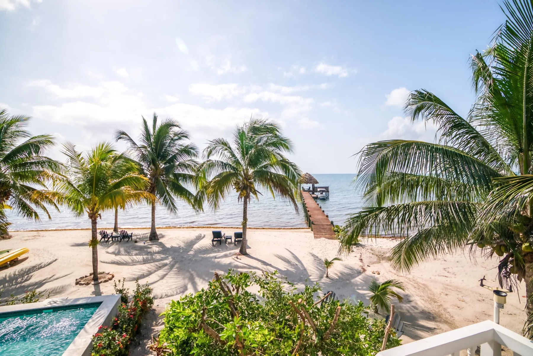 A tropical beach with palm trees, sandy shore, and a walkway extending over the water.