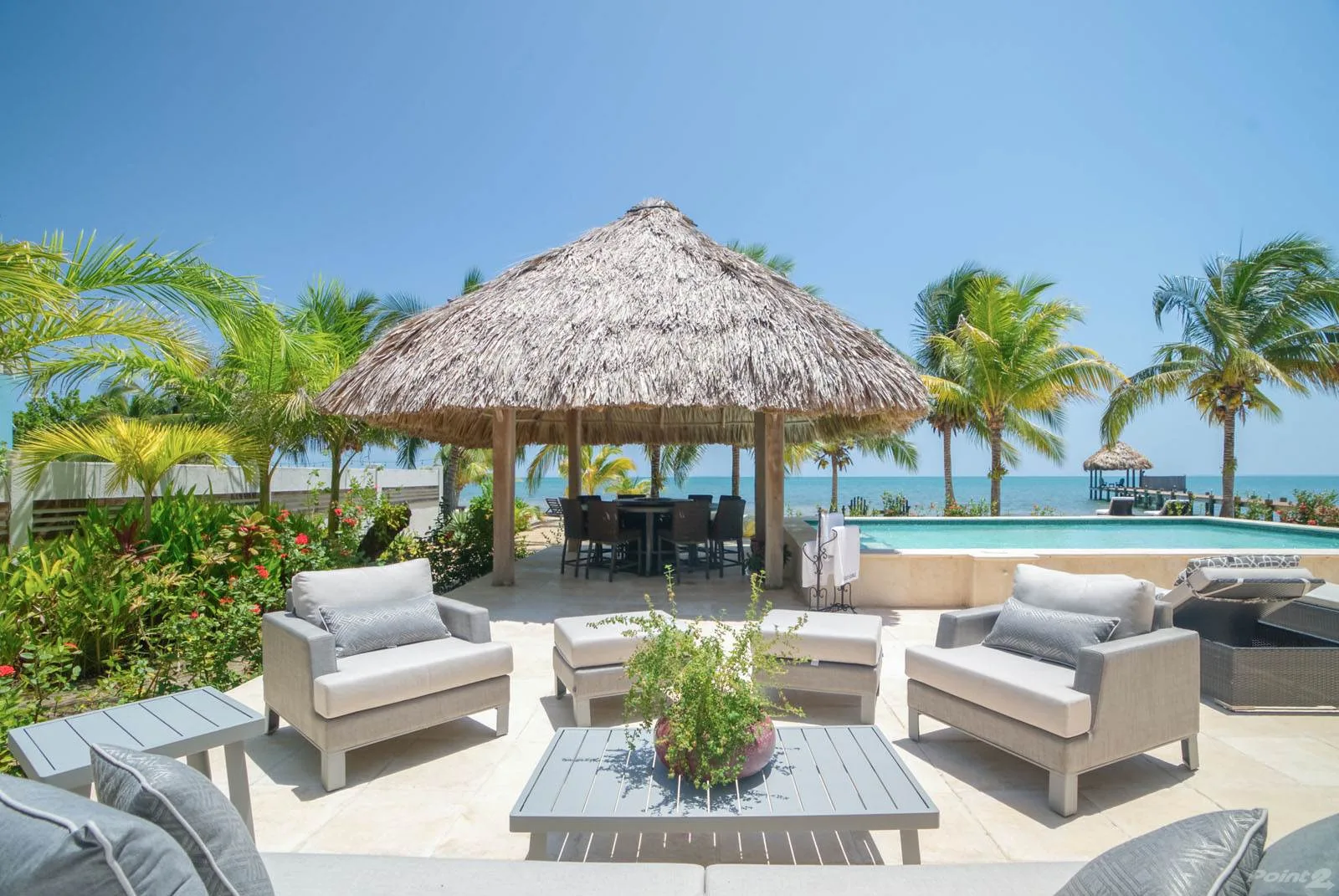 A tropical outdoor seating area with a thatched pavilion beside a swimming pool.