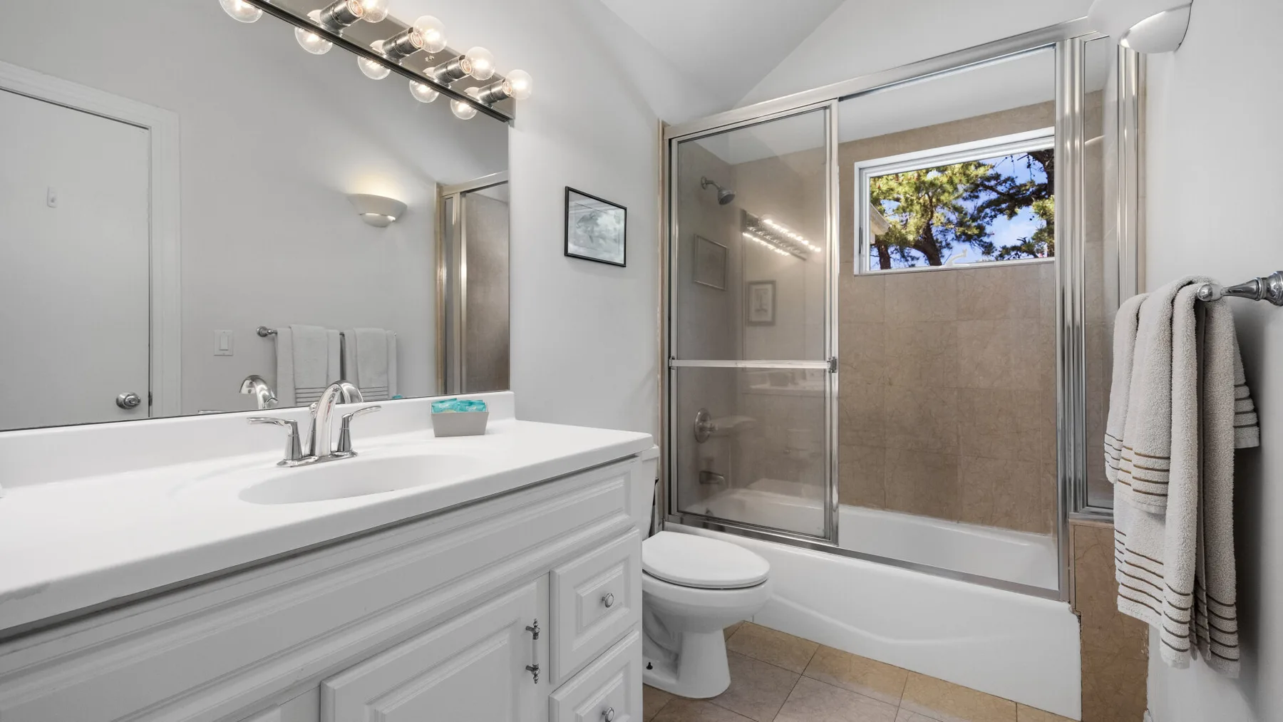 A bright bathroom with a vanity, toilet, and glass-enclosed shower.