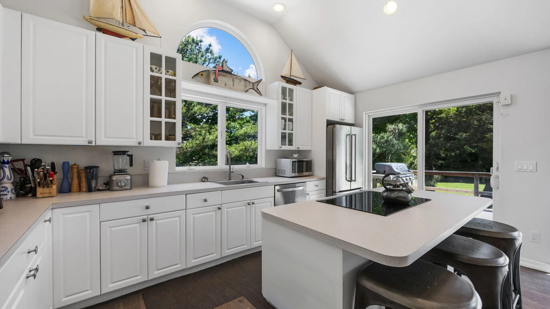 A bright kitchen with white cabinetry, a central island, and large windows overlooking greenery.