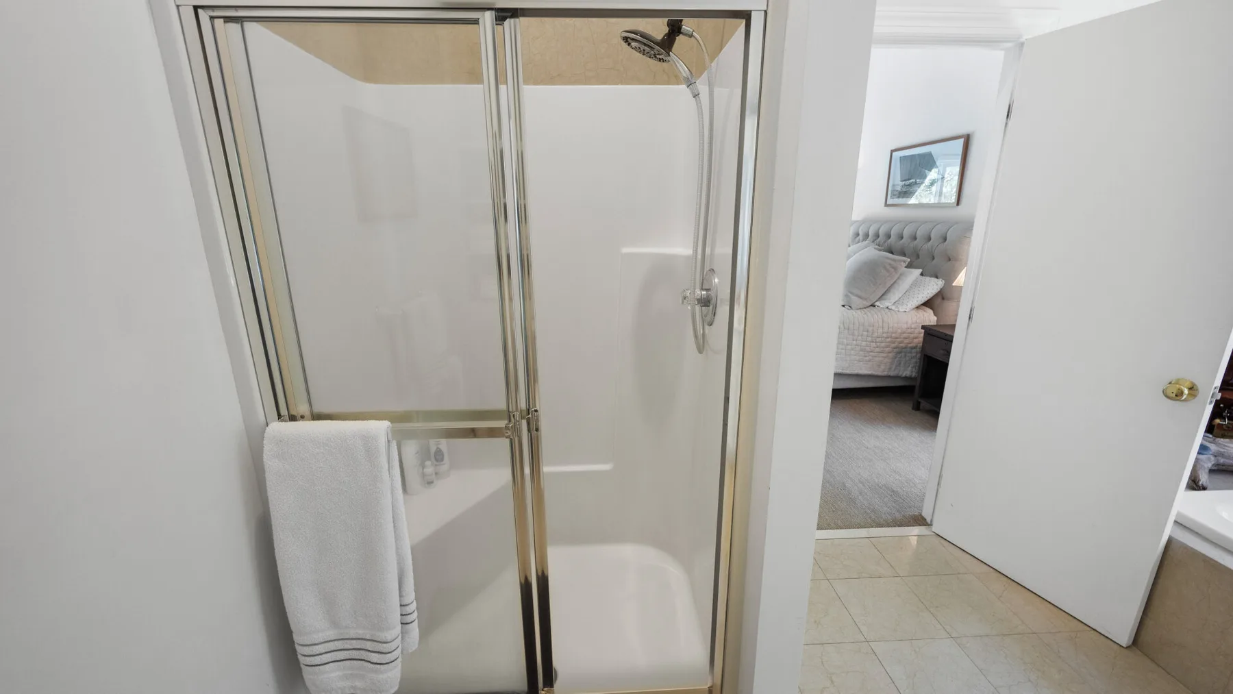A bathroom shower stands beside an open doorway to a bedroom.
