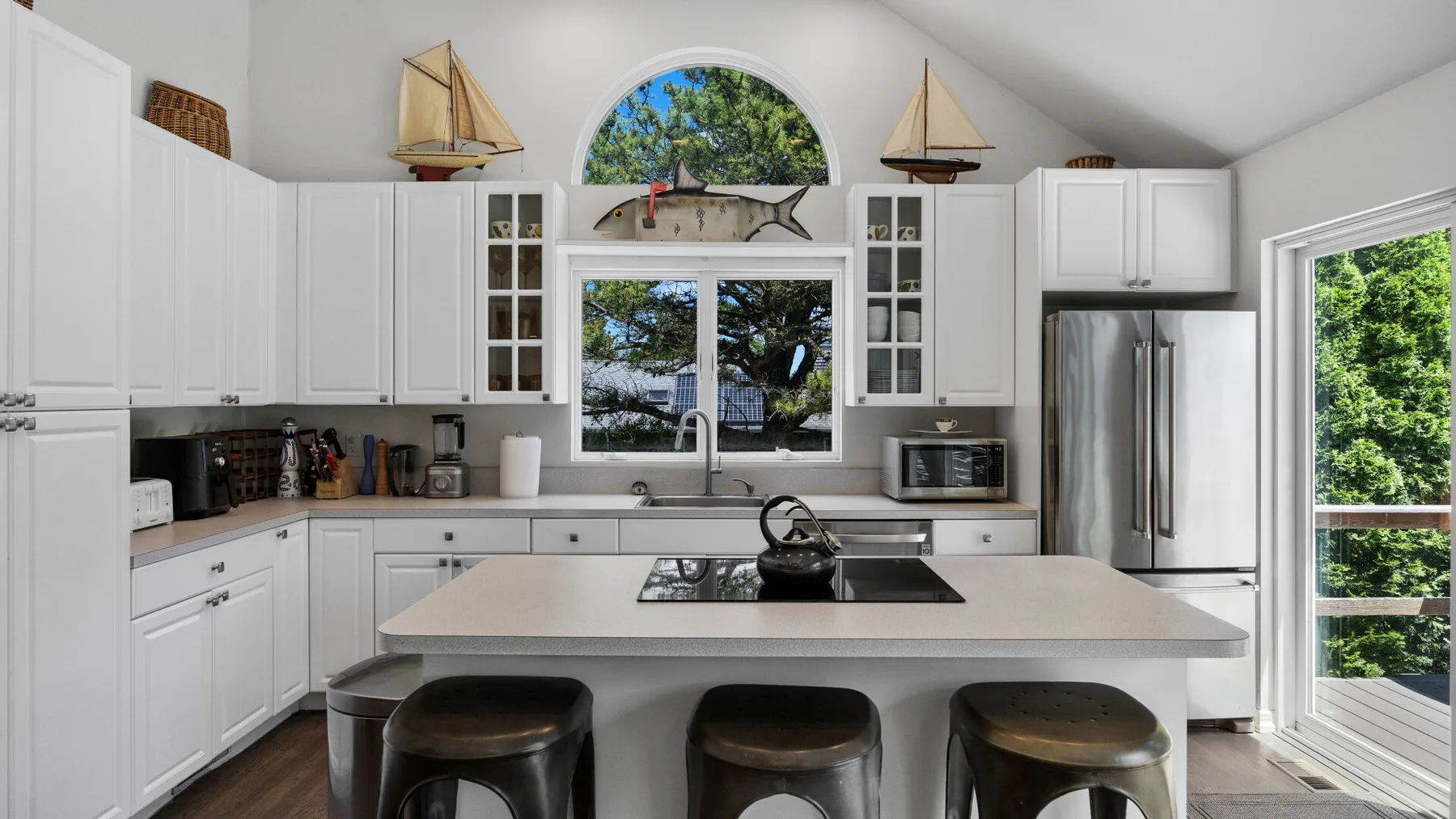 A bright kitchen with white cabinets, a central island, and windows overlooking greenery.