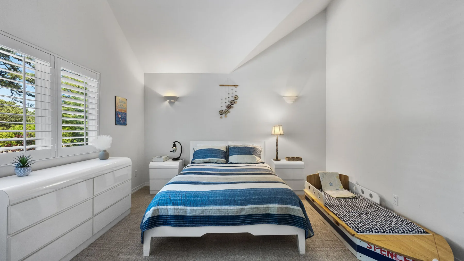A bright bedroom with a blue-striped bed and shuttered windows.