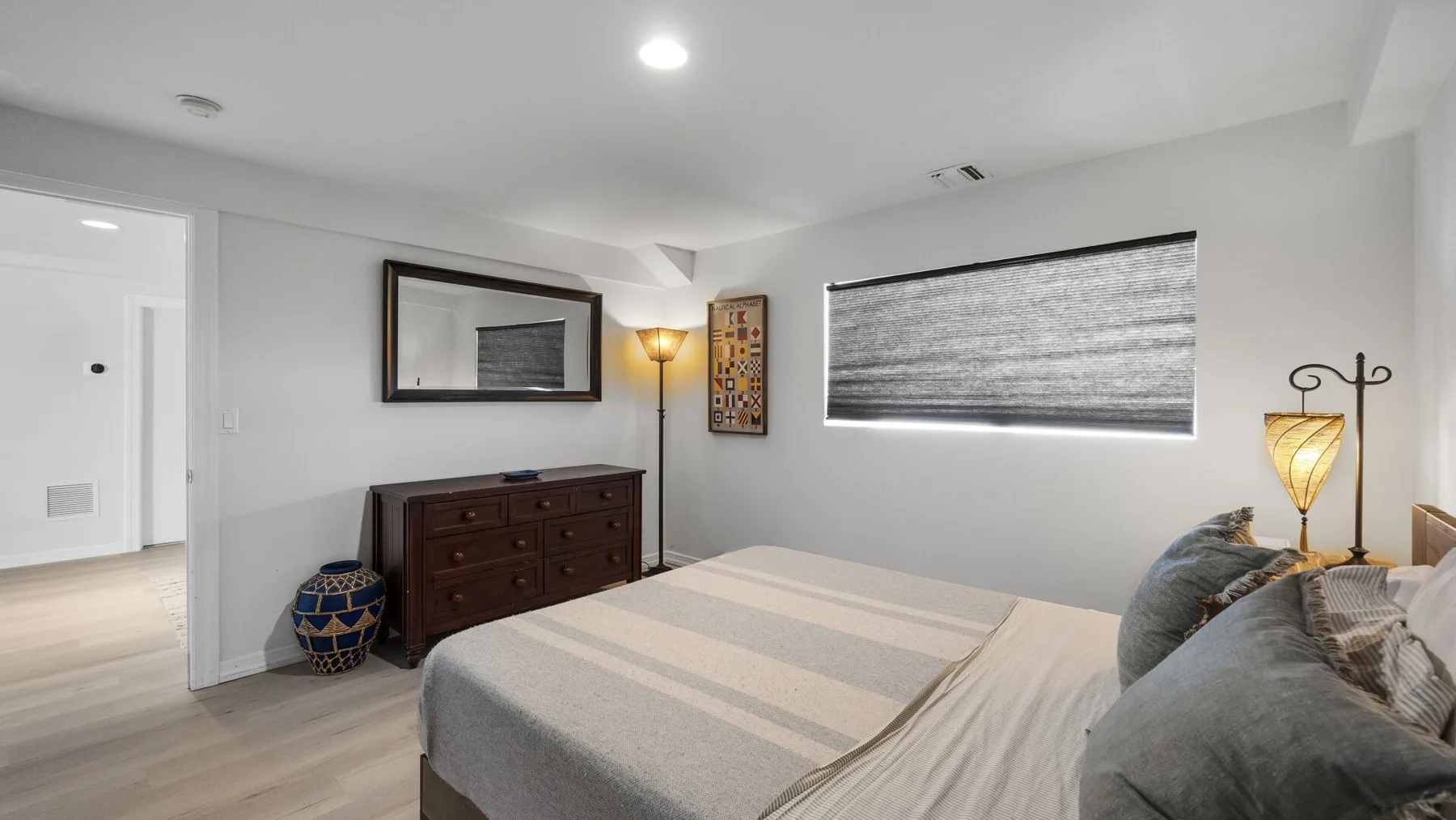 A bedroom with a bed, dresser, and window with a lowered shade.