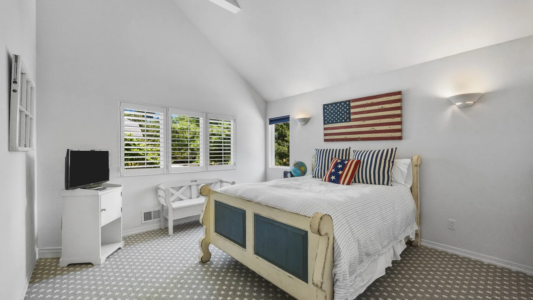A bright bedroom with a bed, striped pillows, and windows with blinds.