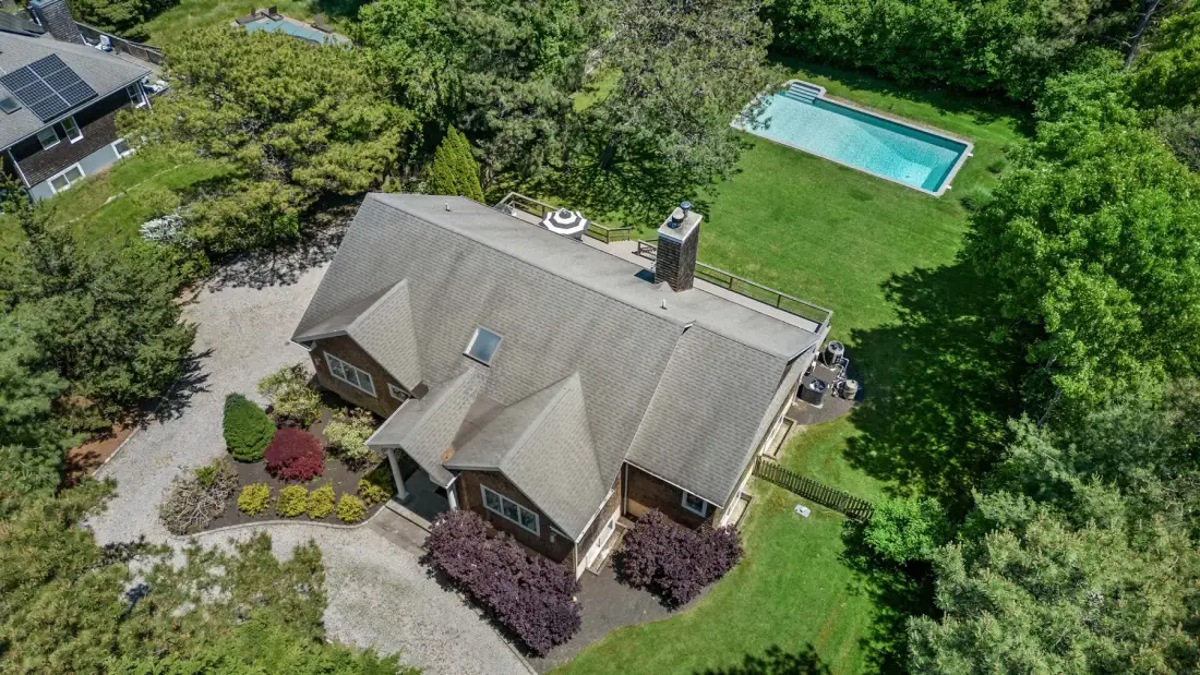 An aerial view of a house surrounded by trees, with a swimming pool nearby.