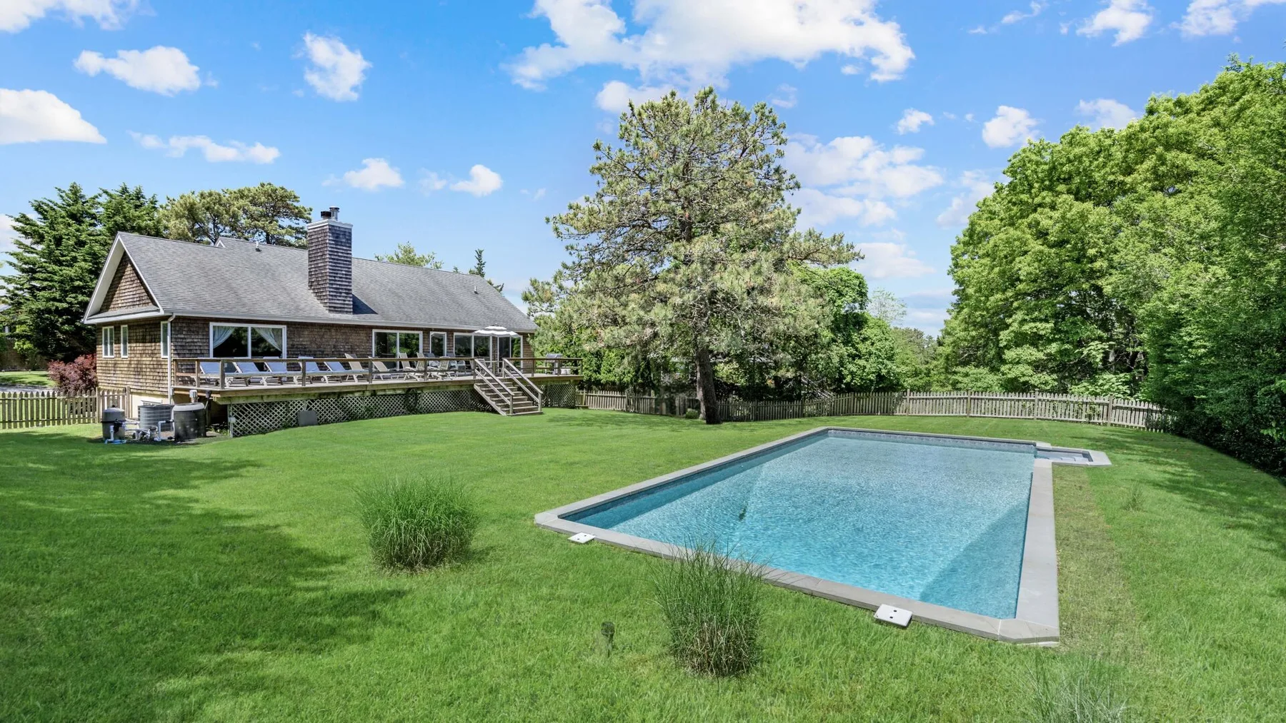 A backyard swimming pool sits in a broad green lawn beside a house.