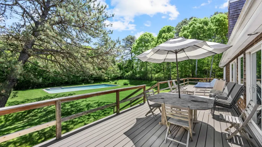 A wooden deck with outdoor seating and an umbrella overlooks a green yard.