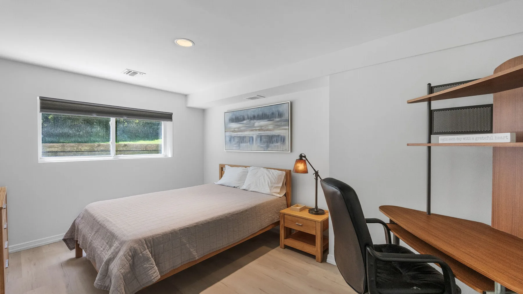 A bedroom with a bed, a desk, and a window.