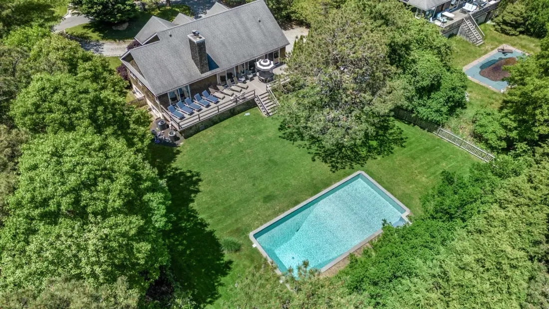 An aerial view shows a house beside a swimming pool and broad green lawn.
