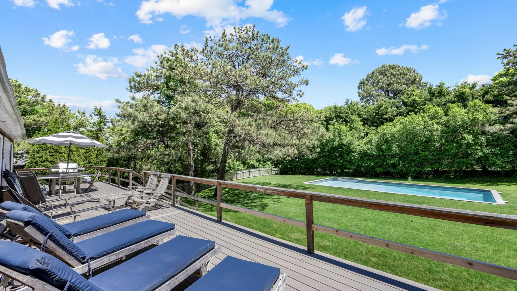 Outdoor deck with lounge seating overlooks a lawn and swimming pool.