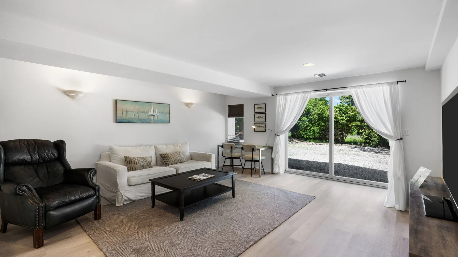 A living room with seating around a coffee table and sliding glass doors opening to greenery.