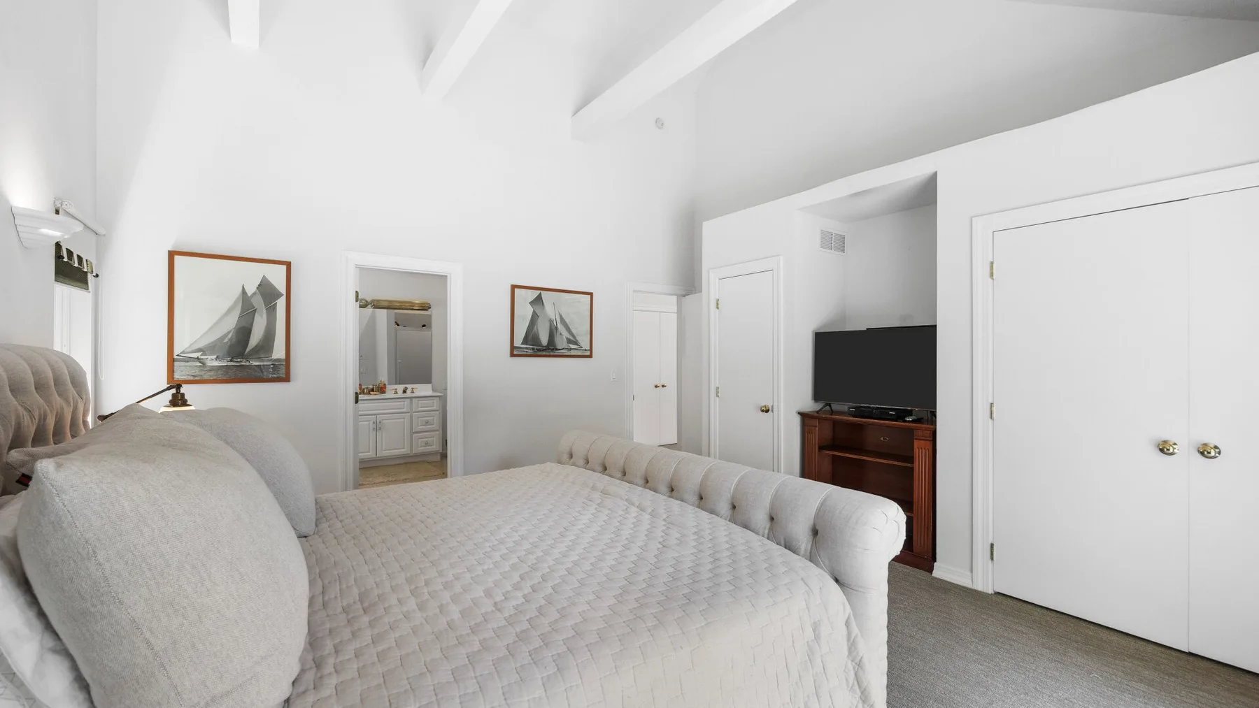 A bright bedroom with a large bed and framed pictures on the walls.