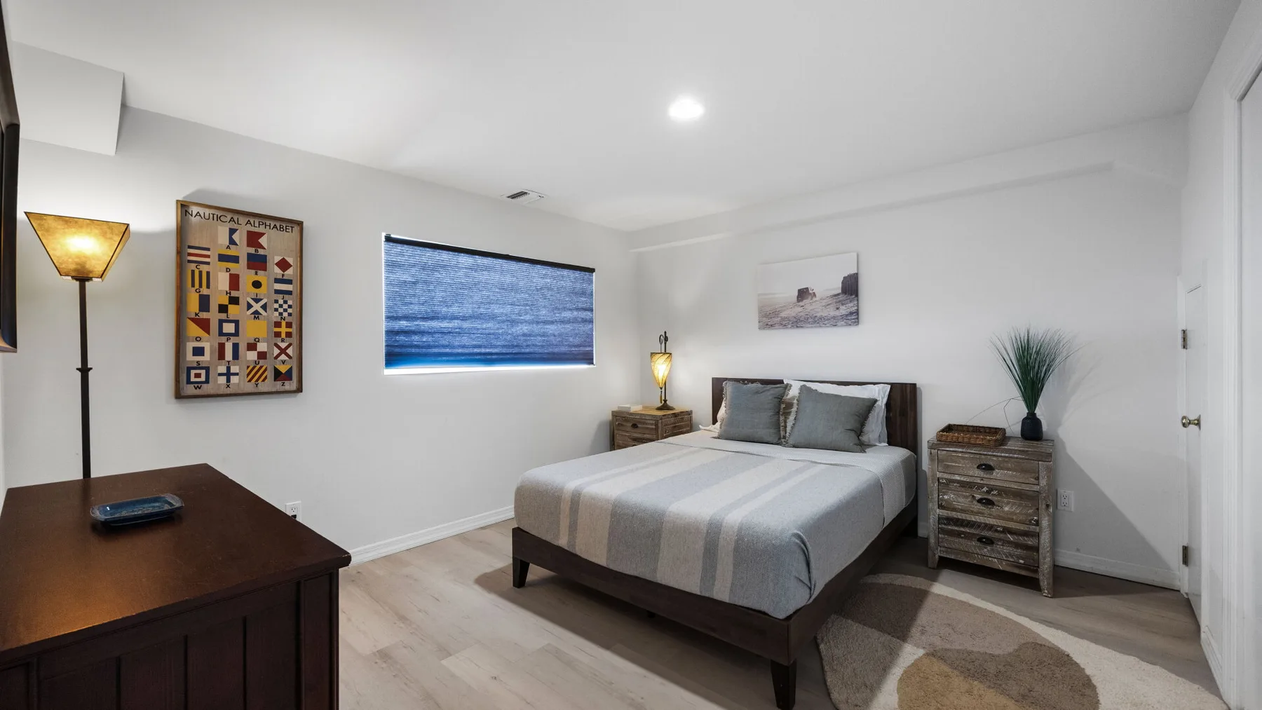 A bedroom with a bed, bedside furniture, and a window with blue blinds.
