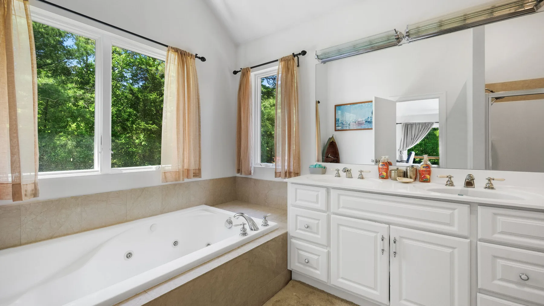 A bright bathroom with a bathtub beneath large windows and a white vanity.