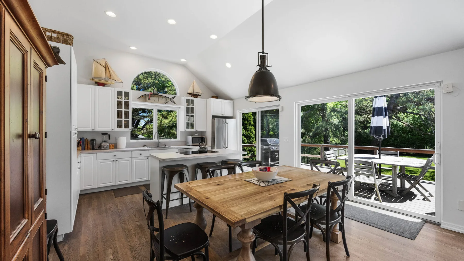 A bright kitchen and dining area with a wooden table beside large windows.