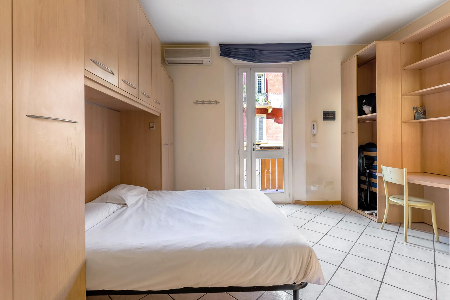 Un dormitorio con una cama, almacenamiento de madera empotrado y una puerta de vidrio al balcón.