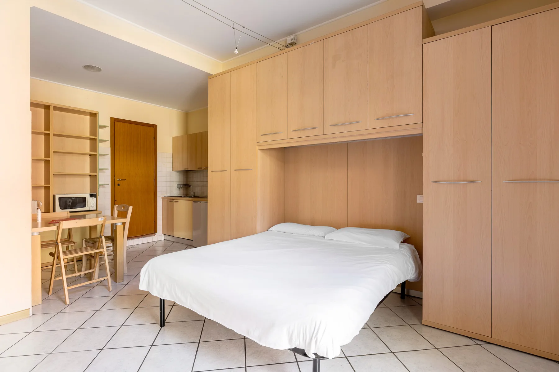 Un dormitorio con una cama, armarios empotrados de madera y una pequeña mesa de comedor.