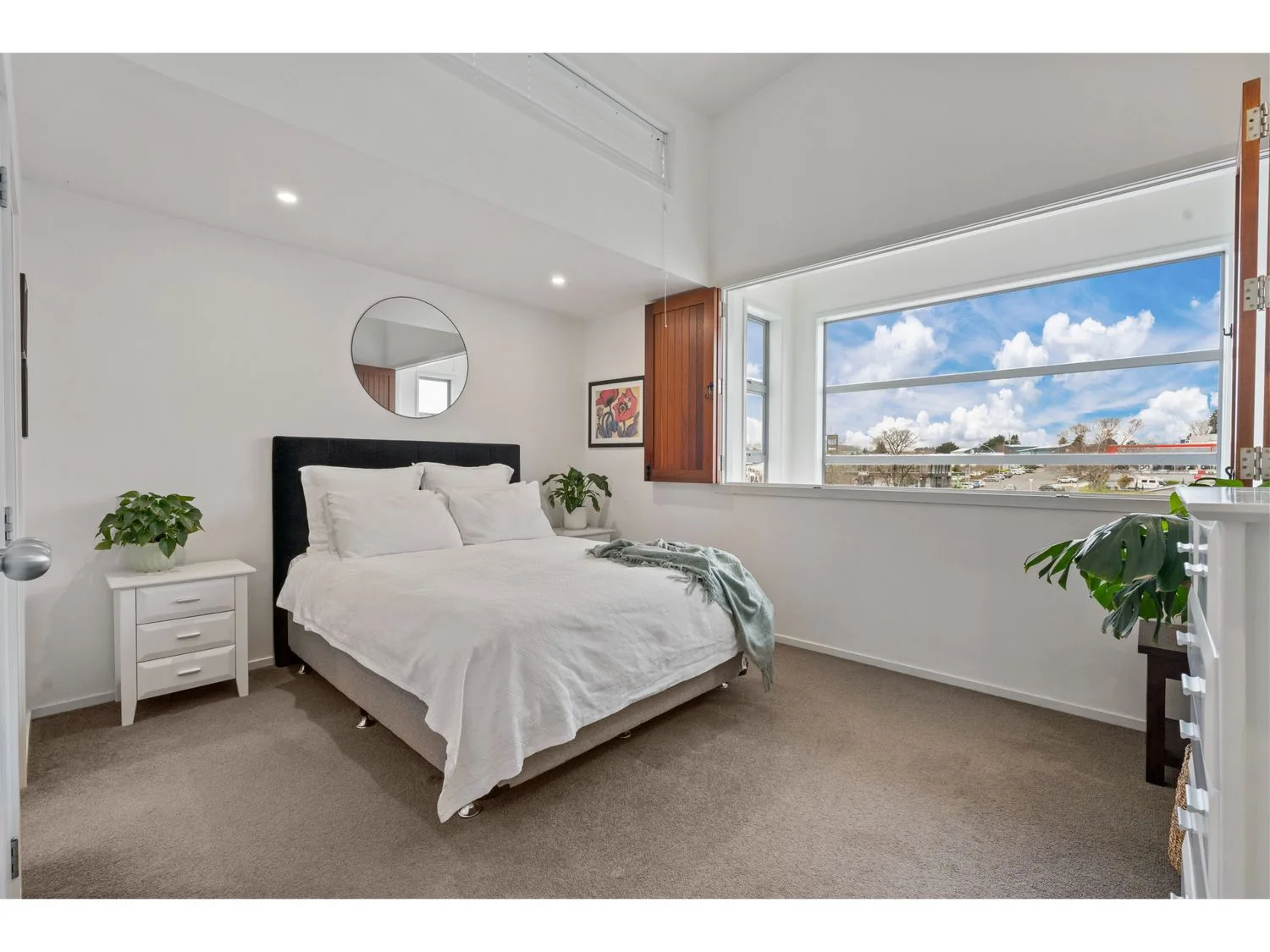 A bright bedroom with a bed and a large window overlooking the water.
