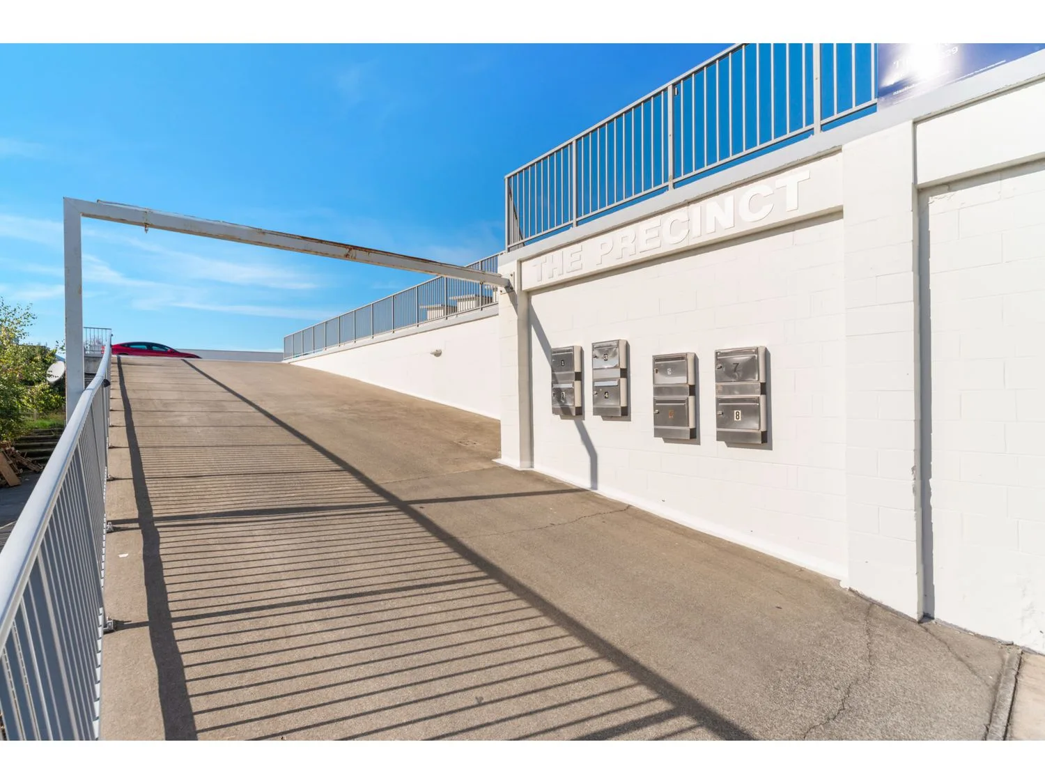 A sunlit outdoor ramp runs beside a white wall with mounted utility boxes.