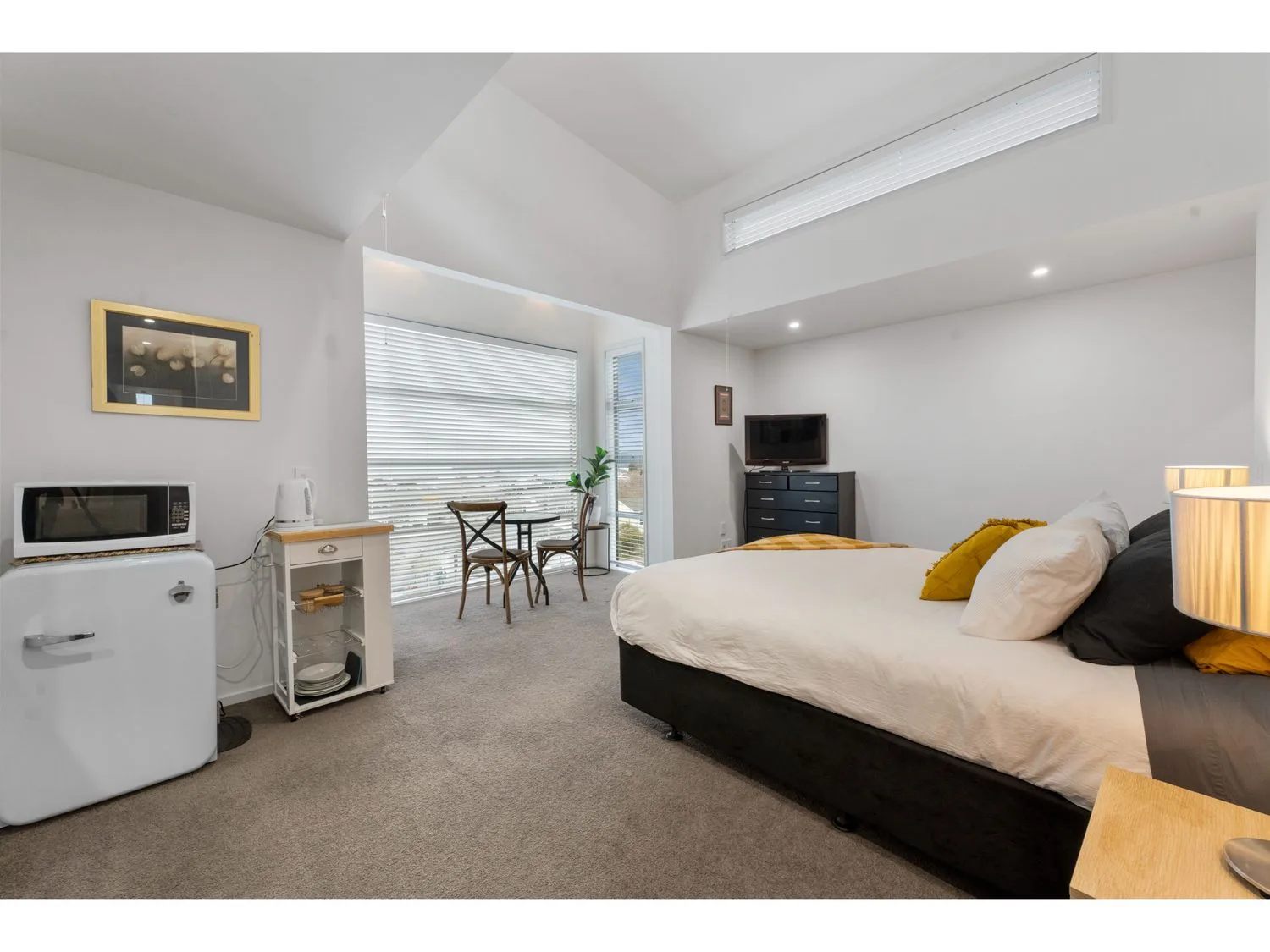 A bright bedroom with a large bed, a small dining table, and a television.