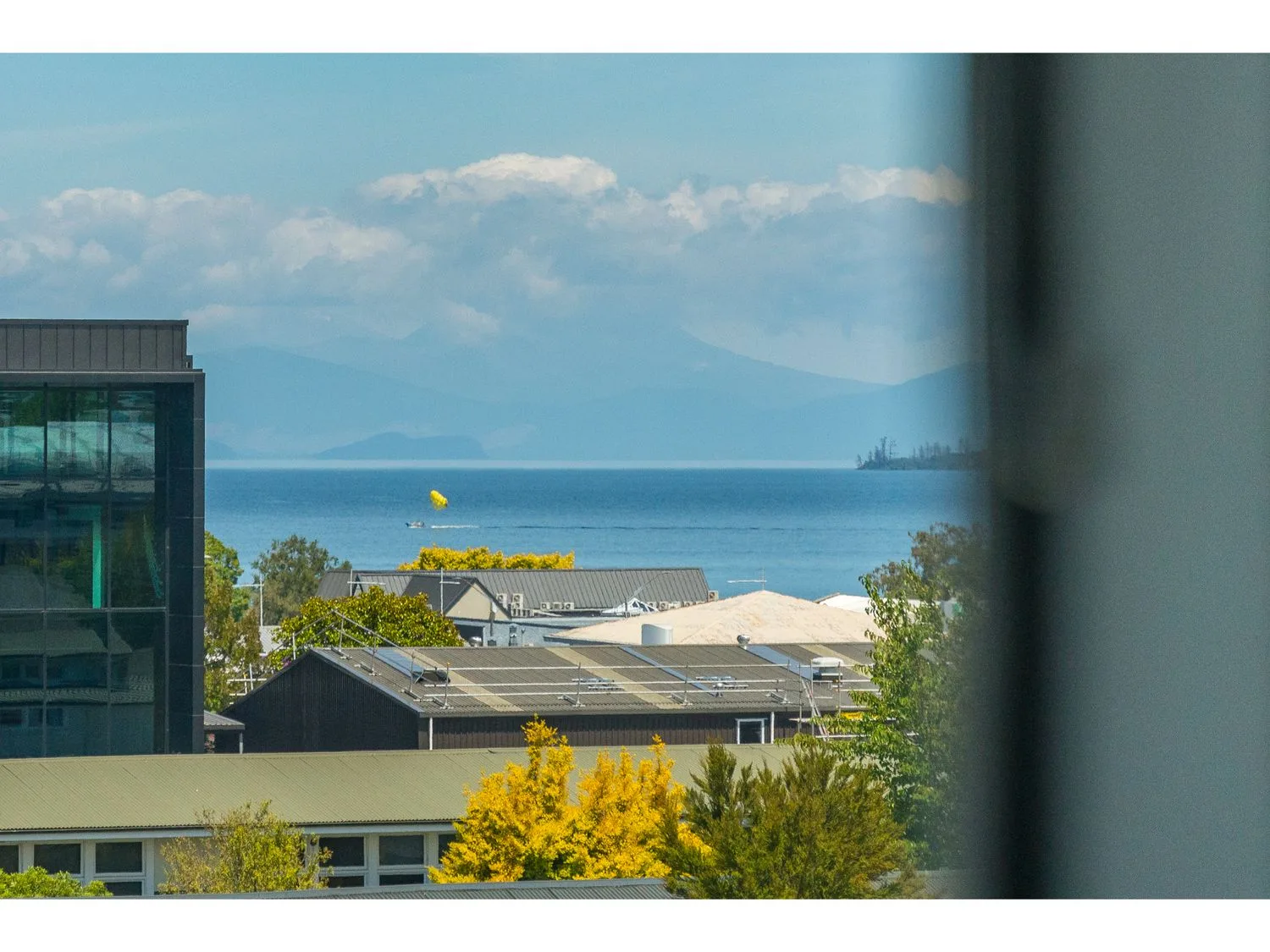 Buildings overlook a blue lake, with distant mountains beneath a partly cloudy sky.