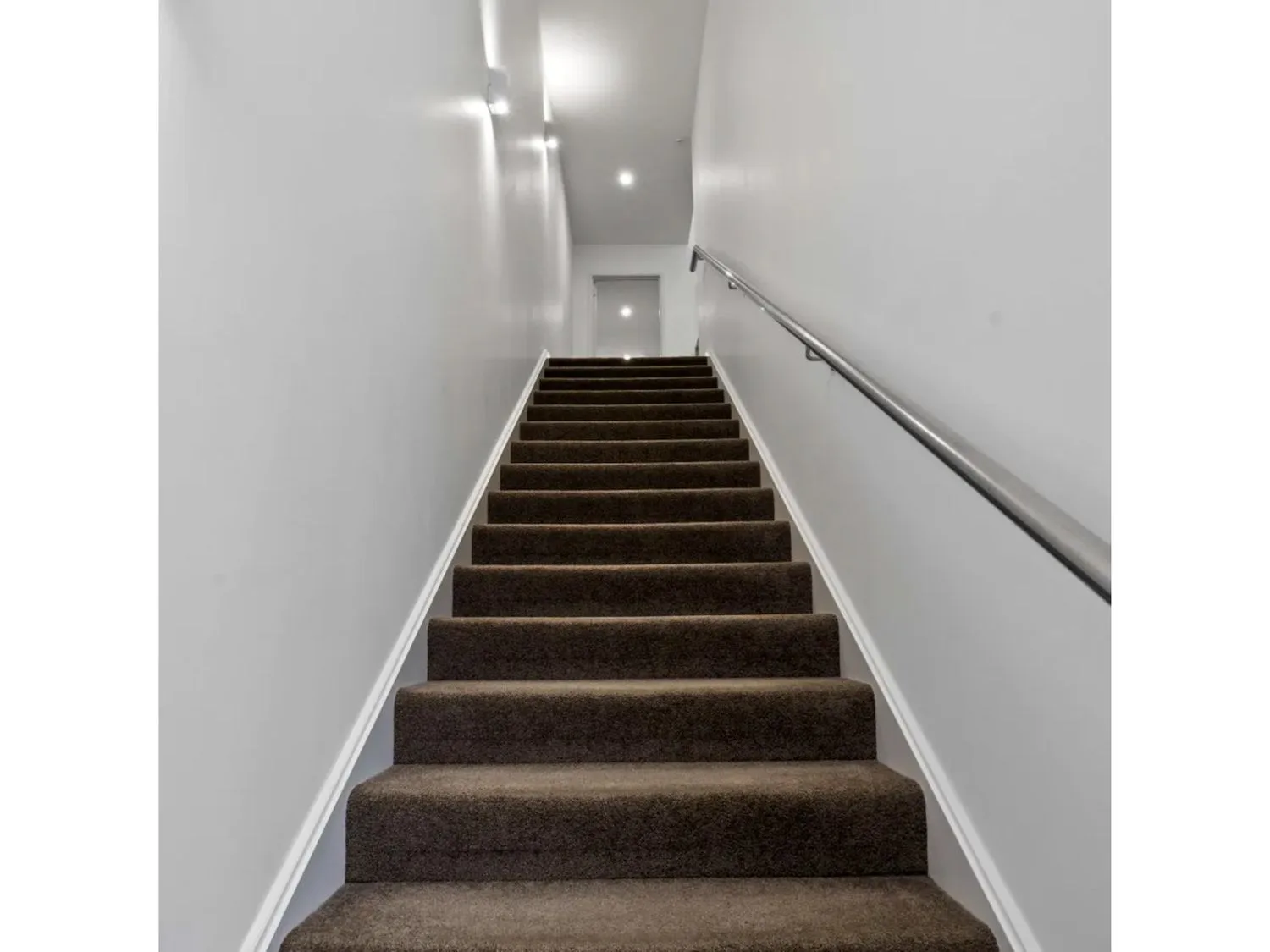 An indoor staircase with a handrail leads toward a door at the top.