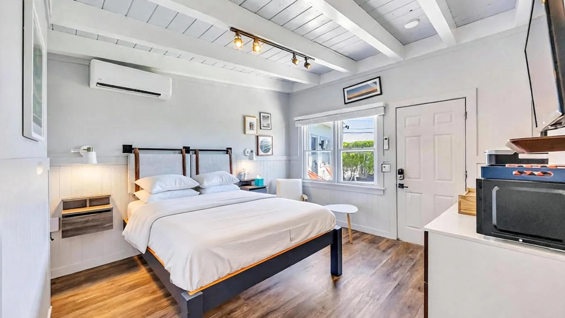 A bright bedroom with a neatly made bed and a window overlooking greenery.