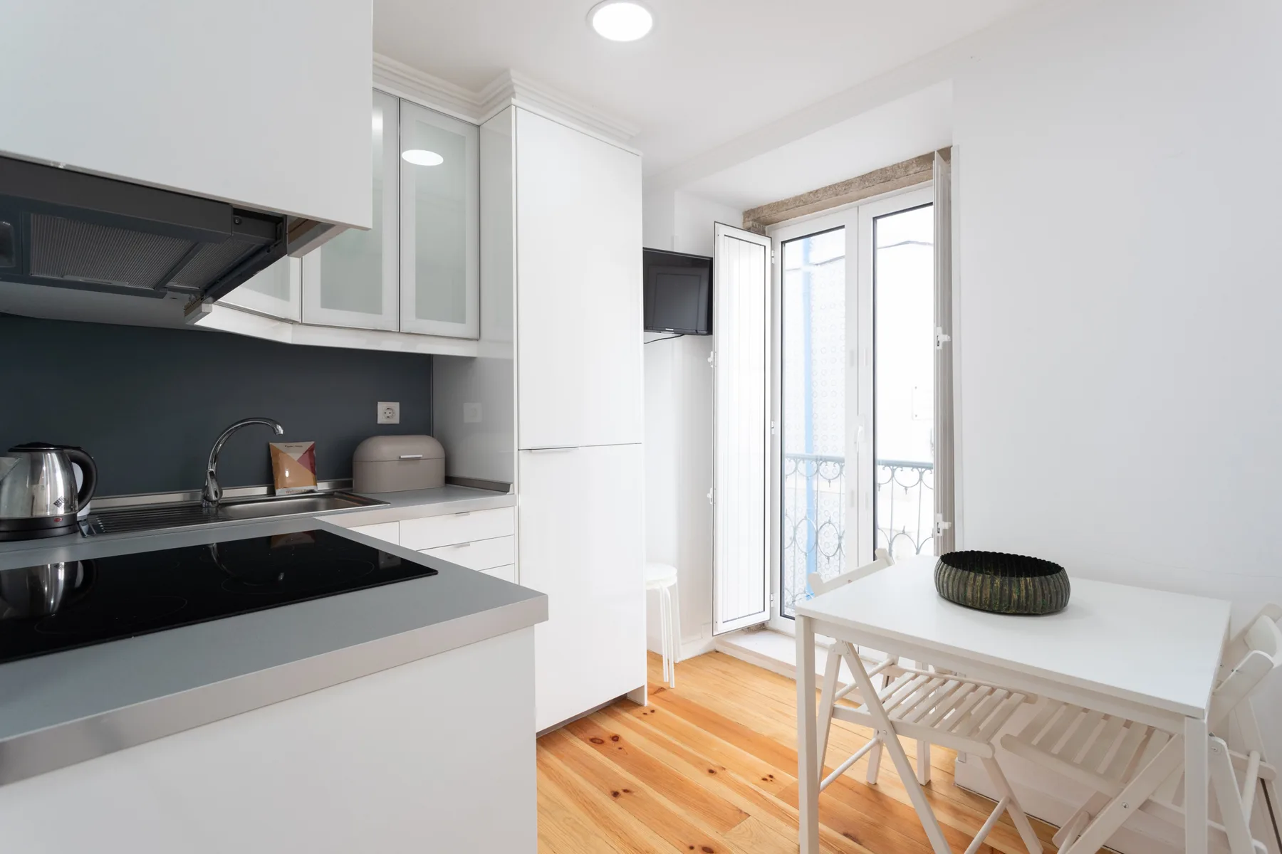 Una cocina luminosa con armarios blancos y una mesa junto a ventanas altas.