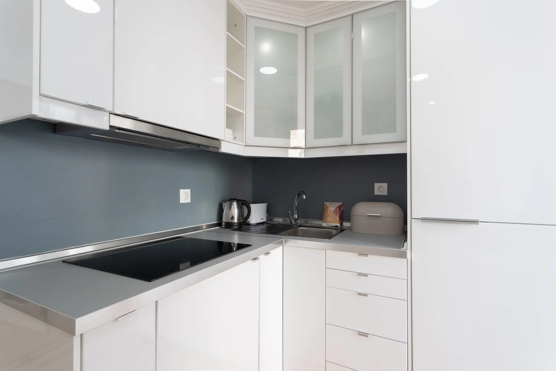 Una cocina moderna con armarios blancos, un salpicadero oscuro y una placa de cocina.