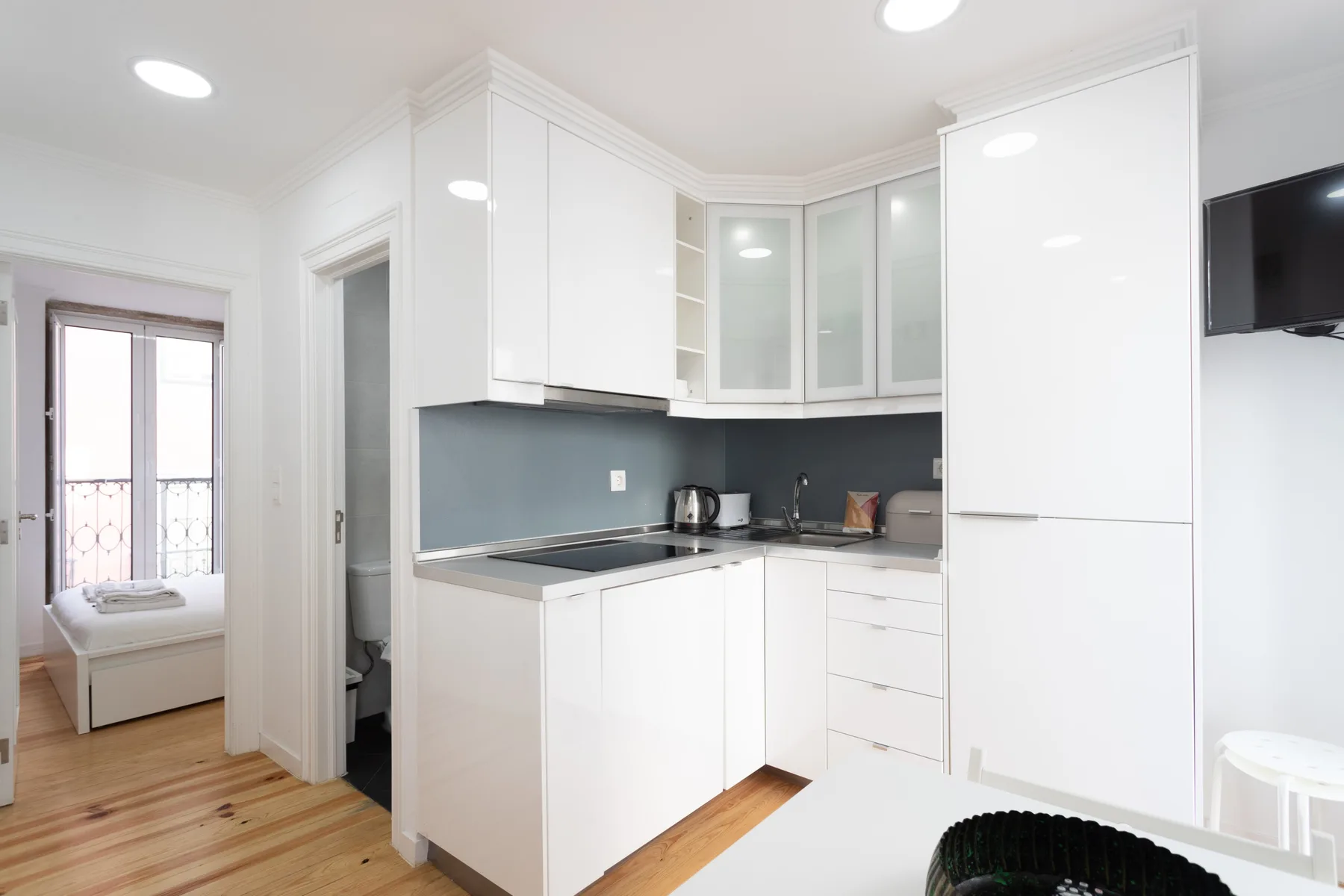Una cocina luminosa con gabinetes blancos, encimeras oscuras y un pequeño televisor en la pared.