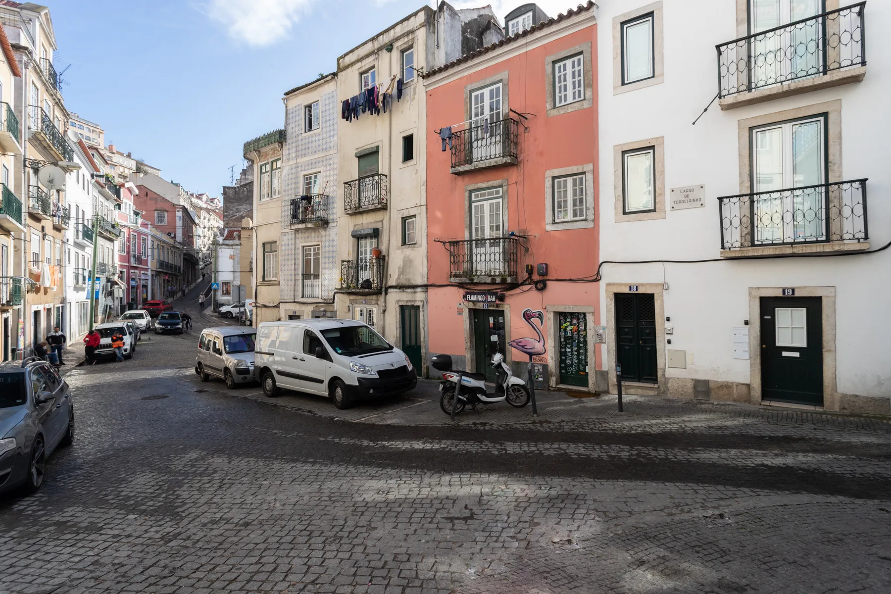 Una calle empedrada bordeada de edificios coloridos y vehículos estacionados.