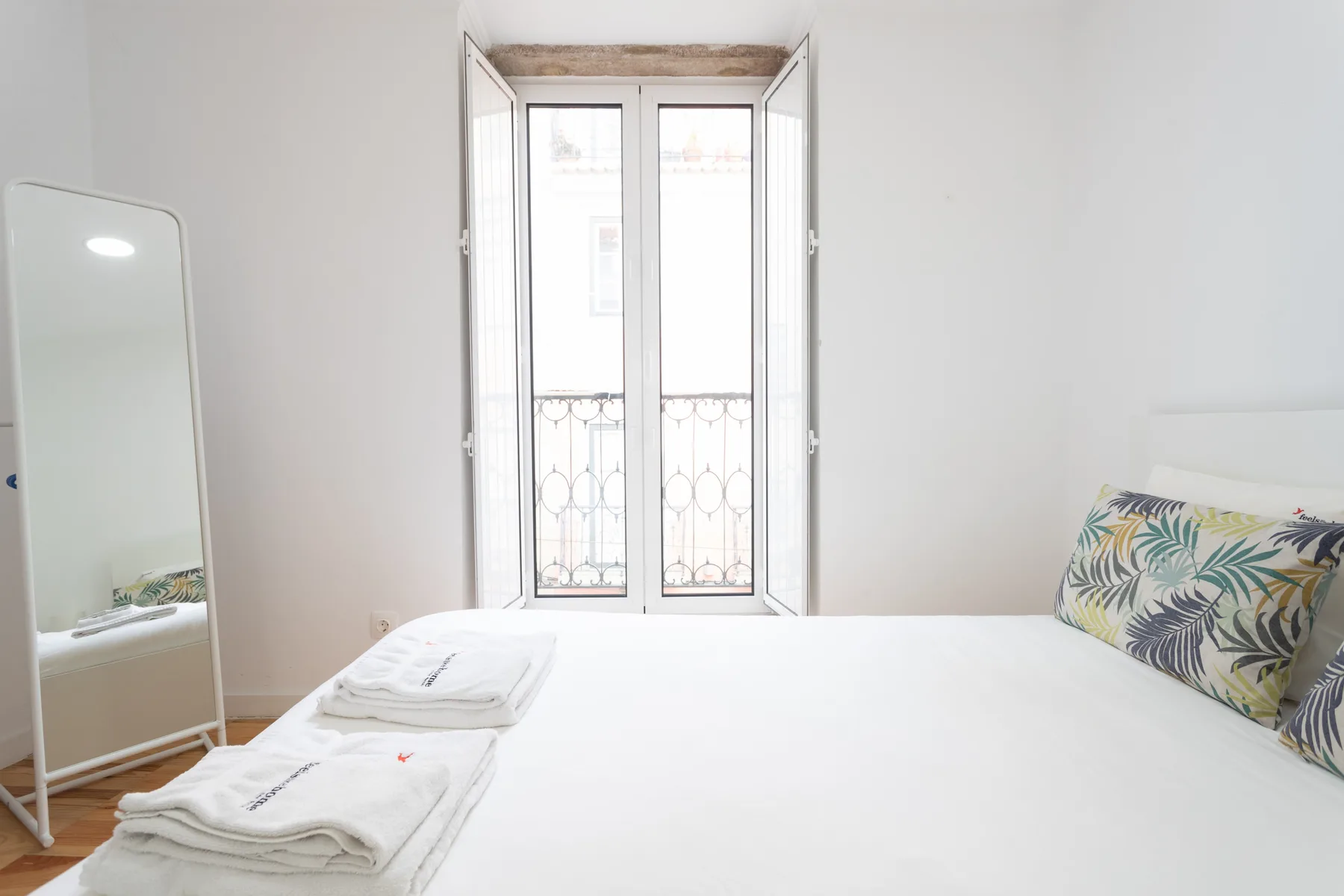 Un dormitorio luminoso con una cama, toallas dobladas y una ventana alta.