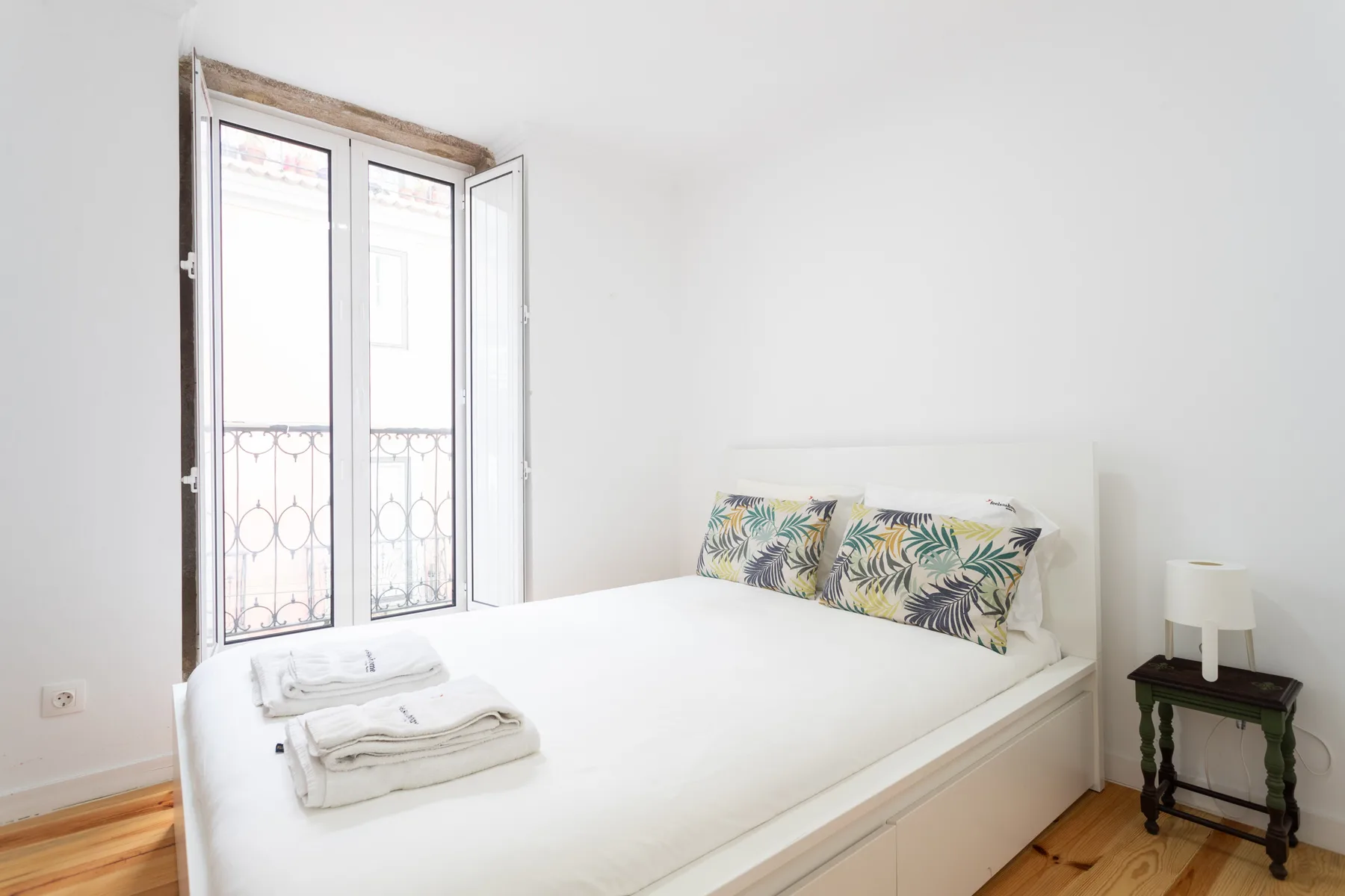 Un dormitorio con una cama blanca junto a una ventana alta.