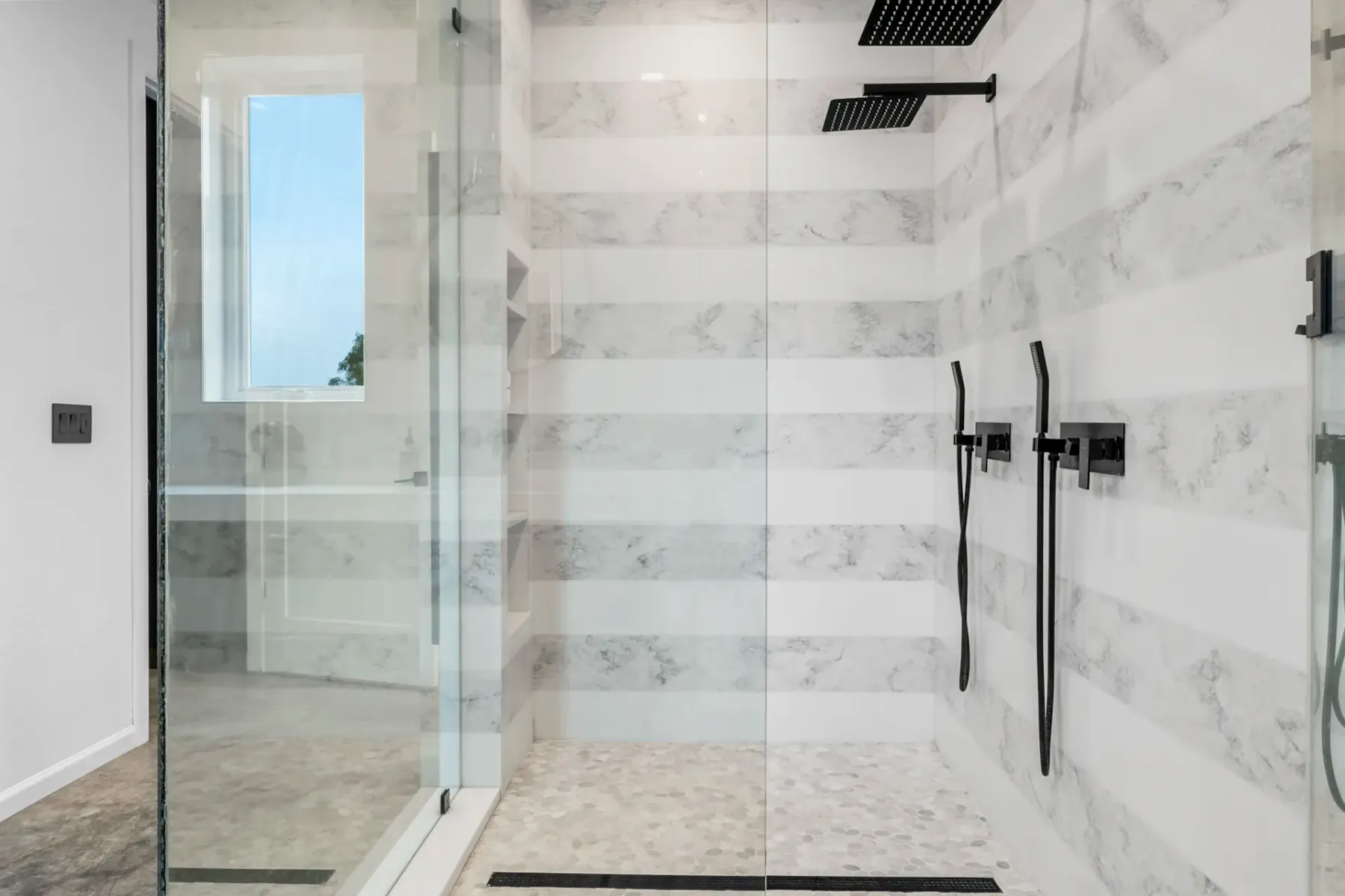 A tiled bathroom shower with glass panels and dark fixtures.