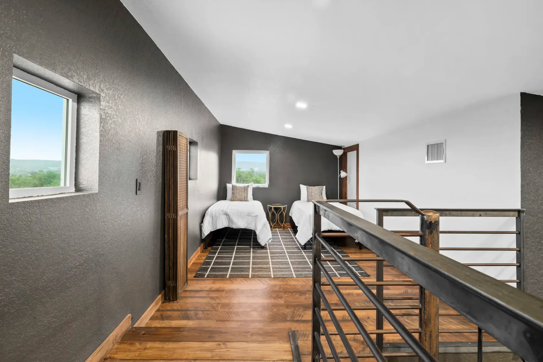 A loft bedroom with two beds, a patterned rug, and a railing overlooking the lower level.
