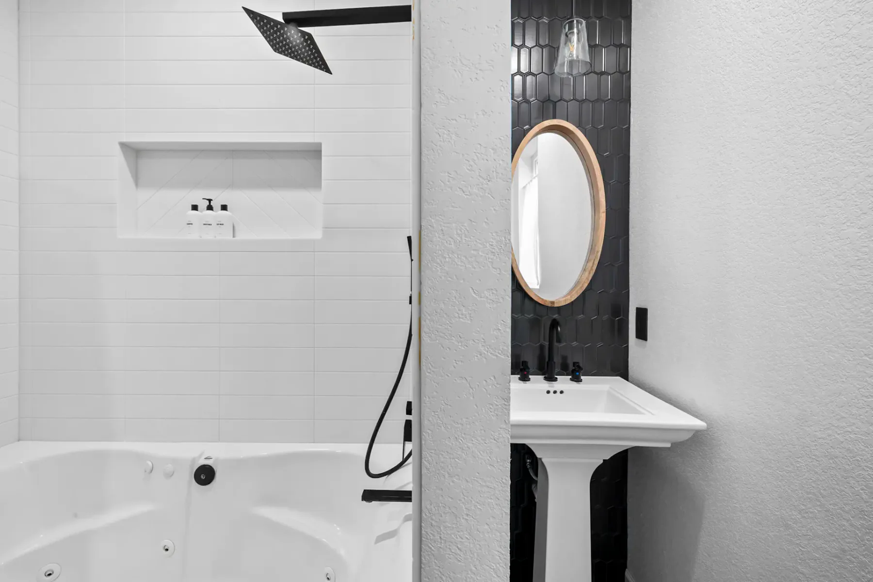 A modern bathroom with a white bathtub and a dark-tiled vanity wall.